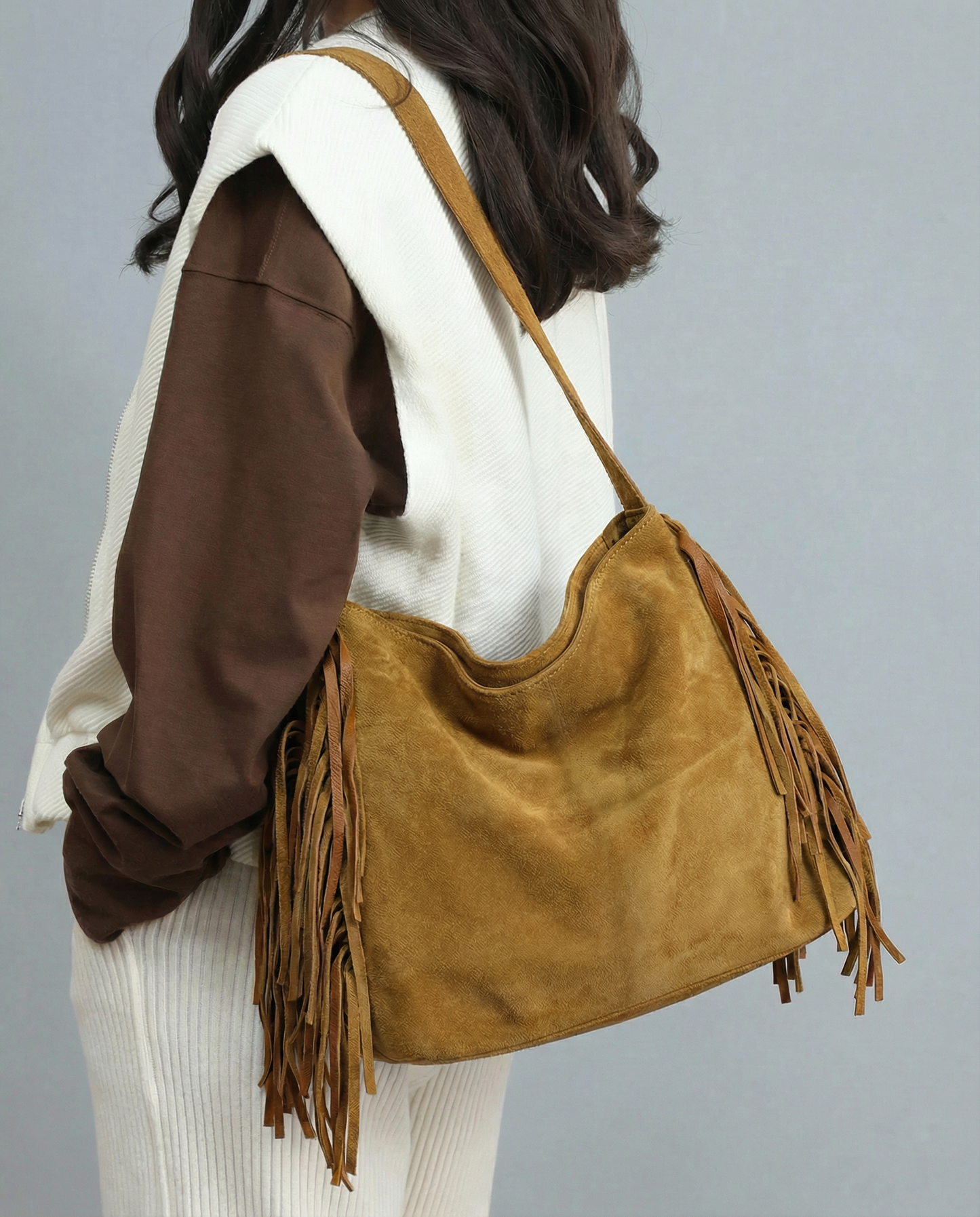 Person wearing a tan suede handbag with fringes on a gray background